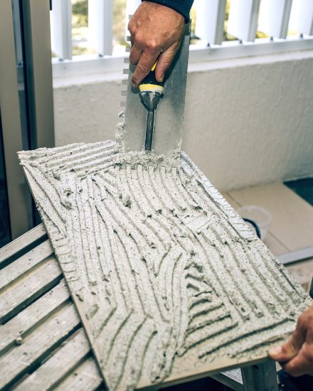 Professional builder smears cement glue on the ceramic tile with a trowel. Concept renovation repair, overhaul, contract tiler.